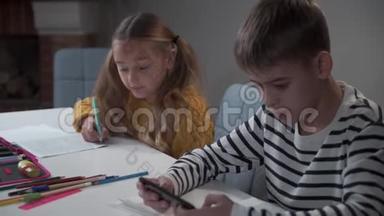 白人男孩在学校或家里玩智能手机游戏。 他的同学或姐姐在<strong>做</strong>作业或<strong>任务</strong>